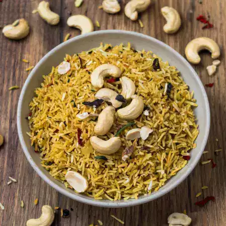Traditional cashew poha breakfast dish served in bowl with roasted cashews curry leaves and fresh lemon garnish