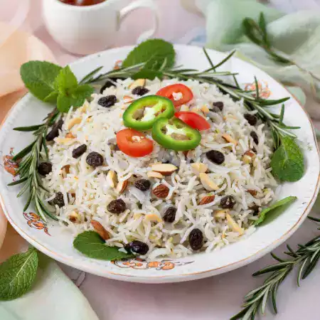Aromatic raisin pulao rice dish garnished with fried onions cashews and golden raisins in serving bowl